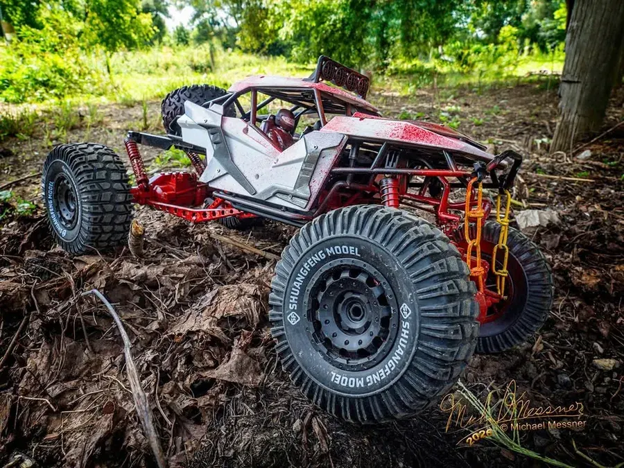 Red and white RC rock crawler buggy navigating rocky terrain with a tow chain at RC World Adventures St. Jacobs
