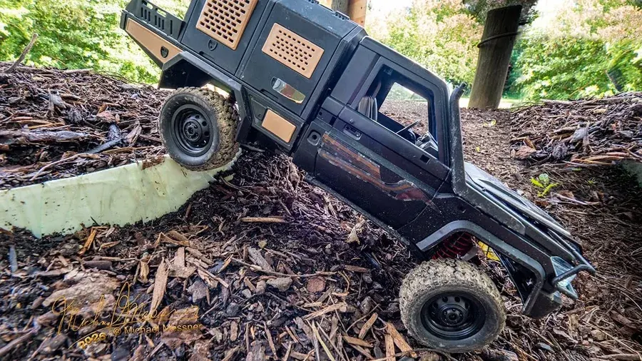 Black RC scale truck crawling up a wood-chip ramp obstacle at RC World Adventures St. Jacobs