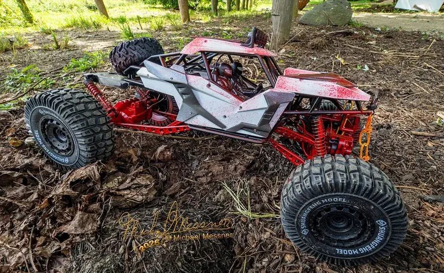 Red and white RC rock crawler buggy climbing packed dirt and leaf-covered terrain at RC World Adventures St. Jacobs